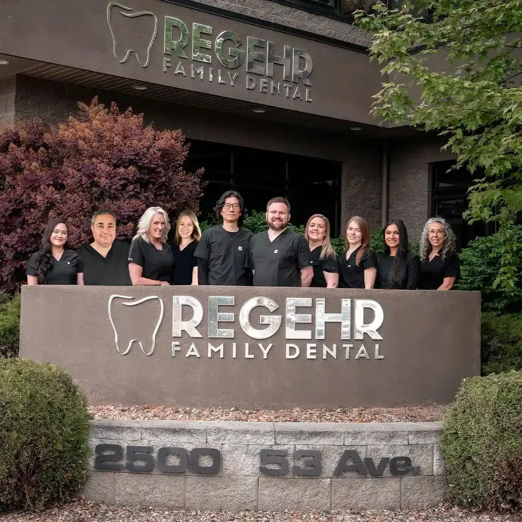 The Regehr Family Dental team standing behind the clinic sign in Vernon